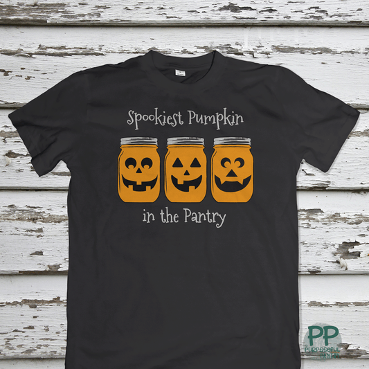 The Printify Toddler Tee Halloween Spookies Pumpkin in the Pantry features three pumpkin faces in jars and festive text—perfect for little ones' Halloween fun.