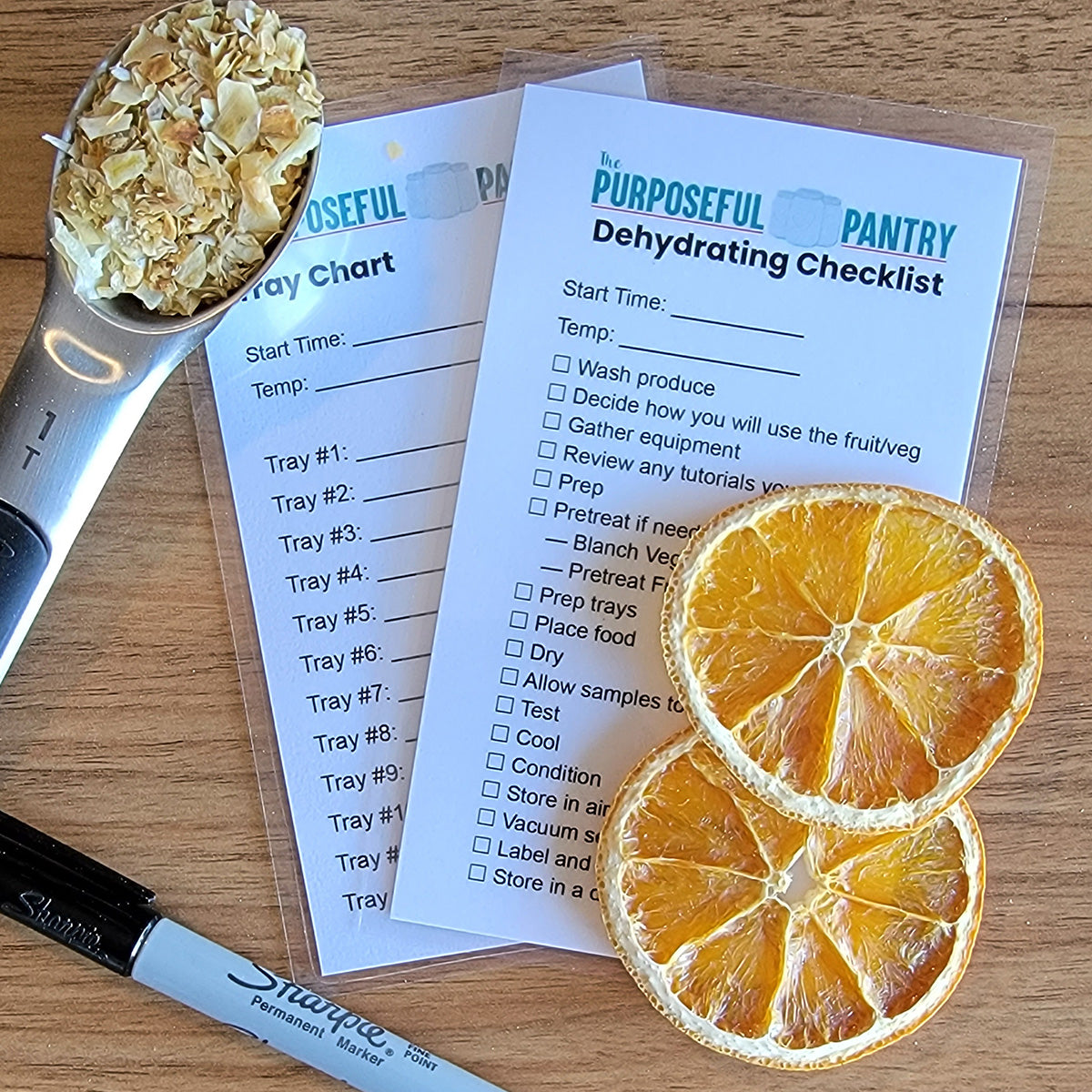 A table with orange slices, a spoon, and a Dehydrating Checklist - Laminated from The Purposeful Pantry.