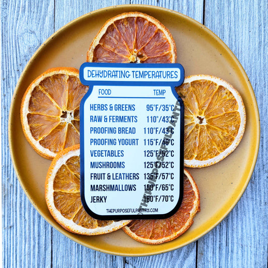 A plate of orange slices with The Purposeful Pantry's Dehydrator Temperature Guide Refrigerator Magnet label on it.