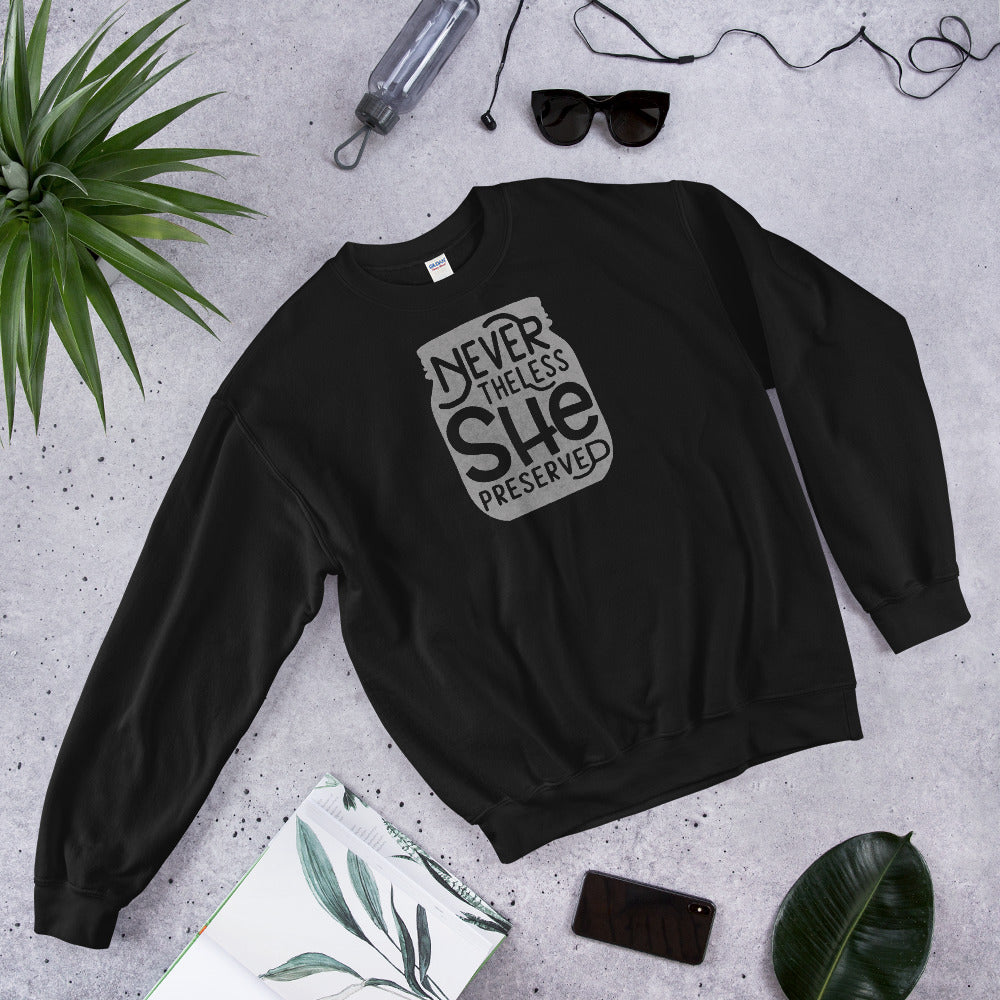 A black Nevertheless She Preserved Comfy Sweatshirt with an image of a jar and a plant next to it, by The Purposeful Pantry.